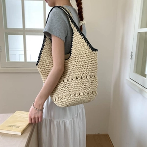Detail of hand-woven straw tote with black contrast trim and hollow-out knit pattern