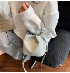 Detail of light blue bucket bag with pebble texture, woven chain, and gold logo