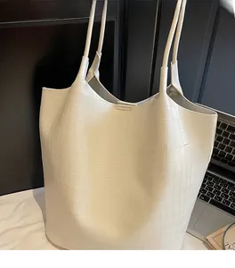 Detail of off-white crocodile embossed tote bag texture on a minimalist office desk