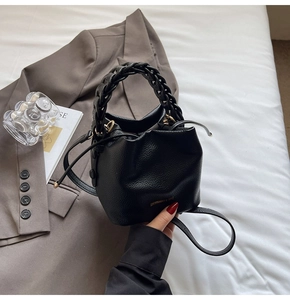 Detail of black textured leather bucket bag with woven handle and drawstring closure