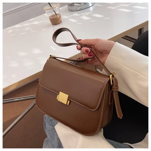 Detail of vintage brown shoulder bag with golden metal square buckle on a white table