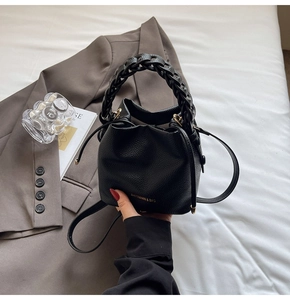Detail of black lychee grain bucket bag featuring a woven handle and gold brand lettering