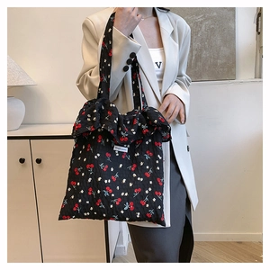 Detail of black canvas tote bag with cherry floral print and ruffle edges on the handle