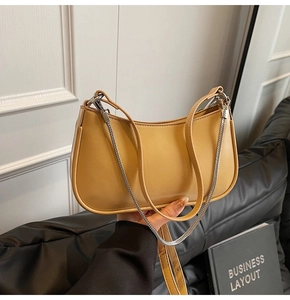 Detail of yellow crescent shoulder bag with leather and silver chain straps on white wall