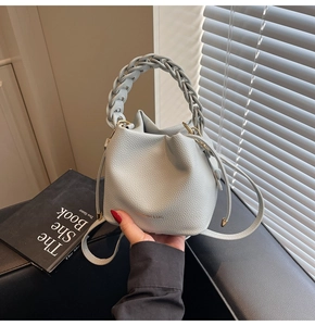 Close-up of light blue pebbled leather bucket bag with braided handle and gold hardware