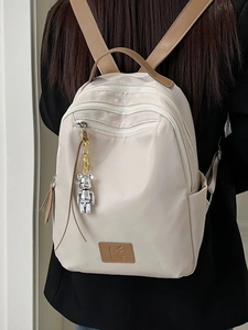 Minimalist beige waterproof travel backpack with brown leather trim and bear pendant charm