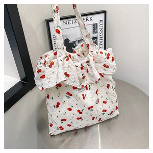 Detail of white mesh tote bag featuring red cherry prints and decorative ruffles