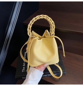 Detail of yellow bucket bag with lychee texture leather and woven handle on books