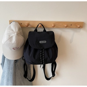 Detail of black nylon drawstring backpack with logo plate and white smiley face baseball cap
