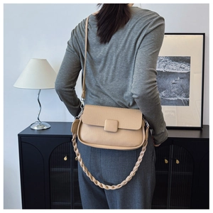 Detail view of beige woven texture shoulder bag with decorative braided handle and flap strap