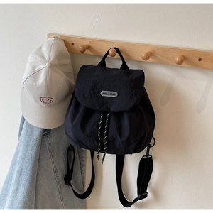 Detail of black drawstring backpack with metal logo plate on a lifestyle coat rack
