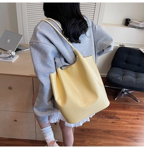Detail of yellow crocodile embossed bucket bag with long shoulder strap in daily use