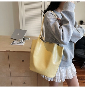 Detail of yellow crocodile texture bucket bag worn by model in a minimalist setting