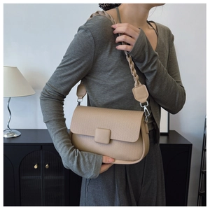 Detail of beige shoulder bag featuring geometric woven texture and leather-wrapped buckle