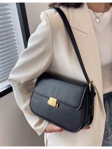 Minimalist black leather crossbody bag with gold buckle on white blazer background