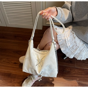 Close-up of a white tote bag featuring silver cross-laces and a pearl butterfly charm