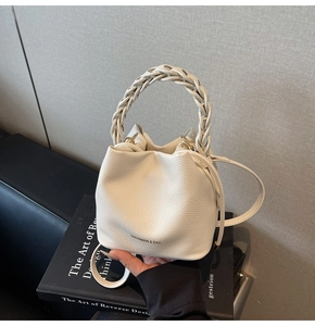 Detail of cream bucket bag showing woven leather handle and pebbled texture finish