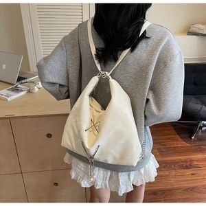 Detail of a creamy white tote bag with metallic chains and a pearl butterfly charm
