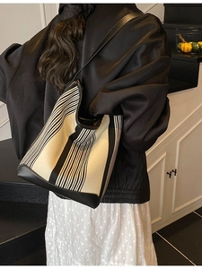 Chic black and white striped tote bag with leather trim worn on the shoulder by a model