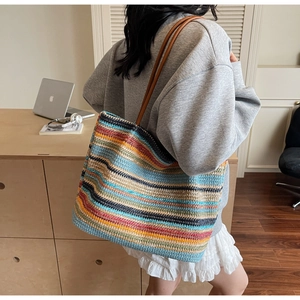 Fashionable rainbow striped woven tote bag with brown leather handles worn by a model