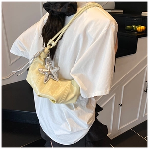 Détail du sac à bandoulière plissé jaune pâle avec pendentif étoile porté par un mannequin