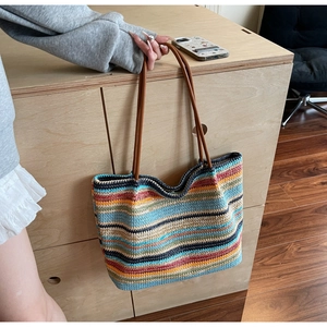 Close-up of colorful striped woven tote bag with brown leather handles on wooden cabinet
