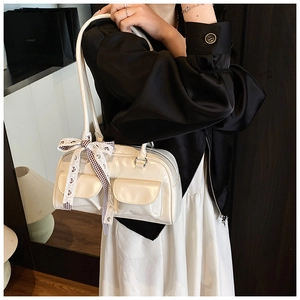 Detail of cream white glossy pillow bag featuring front pockets and checkered ribbon