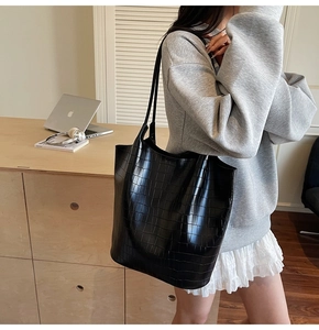 Detail of black croc-embossed tote bag with shoulder straps in a modern office setting