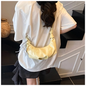 Détail du sac demi-lune en cuir verni jaune avec bandoulière nouée et breloque argent