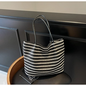 Detail of a large woven tote bag with black and white stripes and leather handles