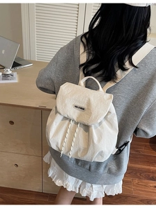 Minimalist beige drawstring backpack made of textured fabric worn by model outdoors