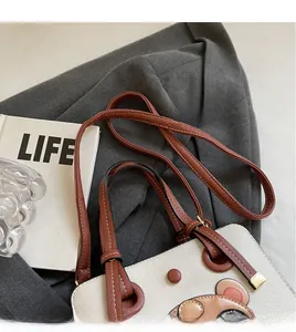 Detail of cream tote bag with cartoon bear patch and brown shoulder strap on gray blazer