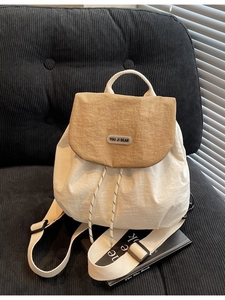 Minimalist beige and khaki bucket backpack with drawstring and handle on black sofa