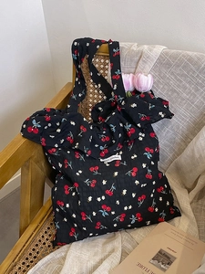Minimalist black mesh tote bag with cherry print and white label on a wooden chair