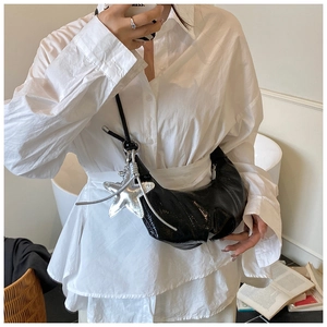 Detail of black patent leather crescent bag featuring a silver star charm and pleat texture