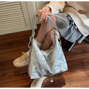 Close-up of silver metallic tote bag with butterfly pearl pendant and chain detail