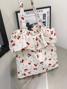 White bubble mesh tote bag with red cherry print and ruffle edge on a metal surface
