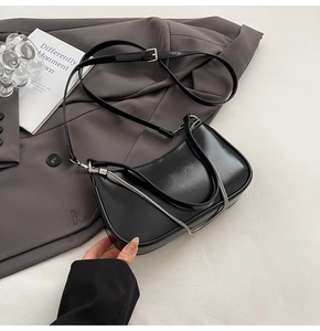 Detail of black glossy patent leather crescent bag with silver chain on a blazer
