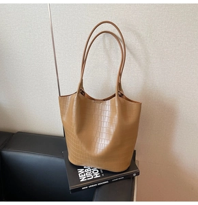 Detailed view of light brown crocodile-patterned tote bag on leather sofa decor