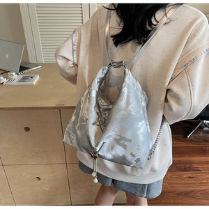 Silver metallic tote bag with pearl pendant detail worn as a backpack in home office