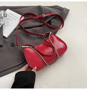 Detail of red crescent shoulder bag with silver chain and adjustable strap on white surface