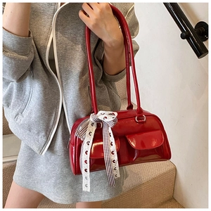 Detail view of red glossy PU leather shoulder bag with a checkered bow ribbon charm