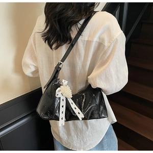 Detail of black glossy patent leather shoulder bag with lace bow and pearl charm
