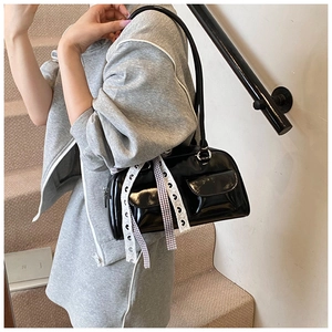 Detail of black glossy patent leather shoulder bag with decorative checkered ribbons