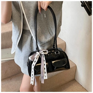 Detail of black glossy patent leather shoulder bag with decorative plaid bow ribbon
