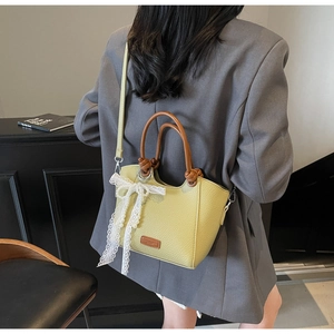 Détail du sac seau en cuir vert clair avec nœud en dentelle et poignées brunes