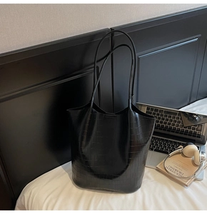 Detail of black crocodile texture bucket bag on white bedding with professional styling