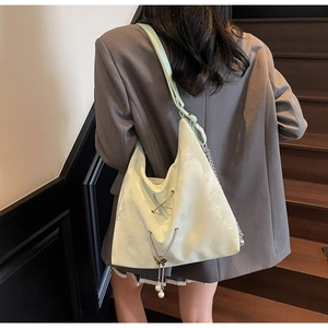 Detail of light green tote bag with metal cross decor and pearl pendant strap