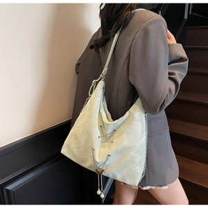 Detail of mint green textured tote bag with metal lace-up design and pearl tassel