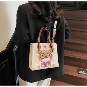 Detail view of cream lychee leather tote bag featuring cartoon cat patch and LOVE wide strap